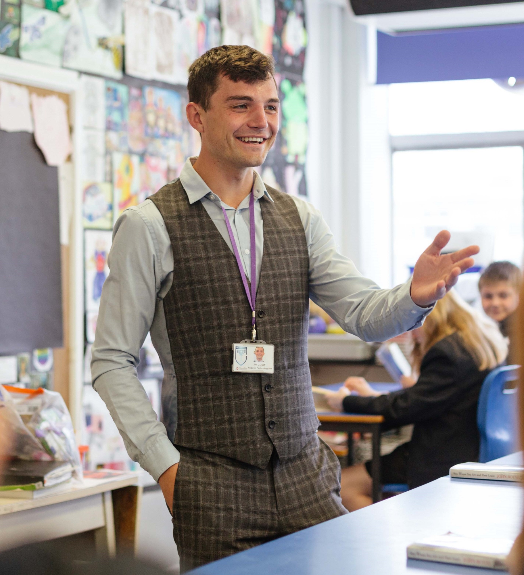 Male teacher standing smiling in front of class with students listening to him