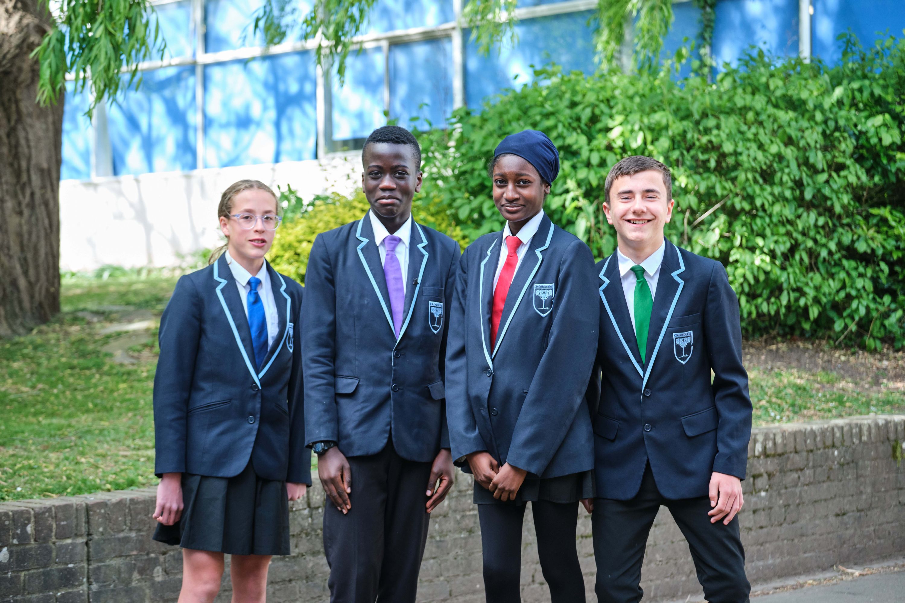 4 students smiling at the camera with different coloured house ties - green, red, blue and purple 