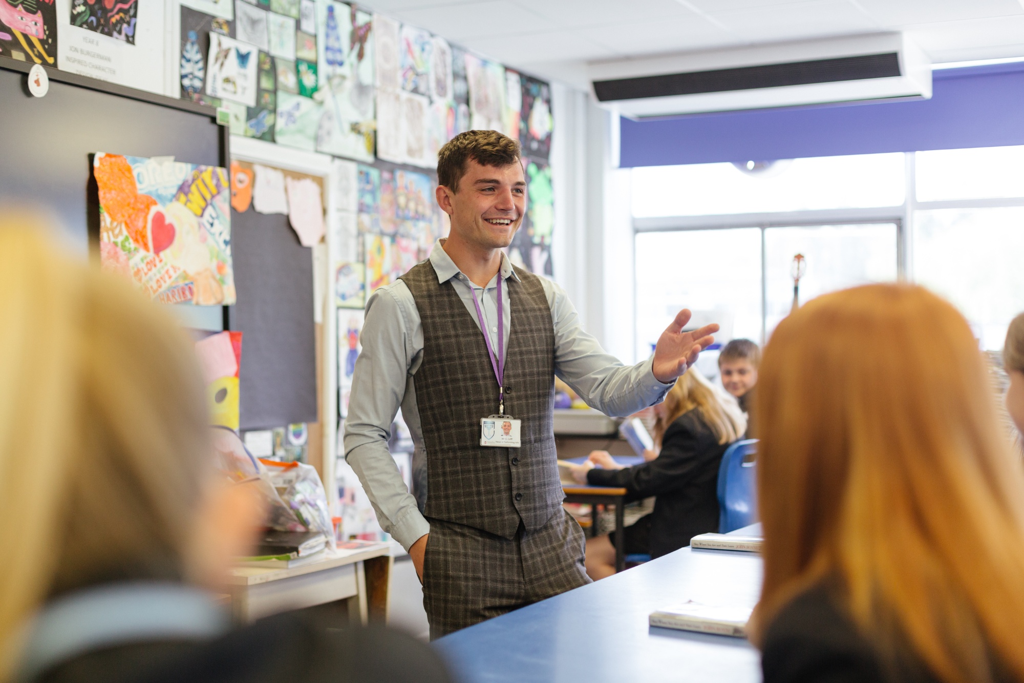 Male teacher standing smiling in front of class with students listening to him